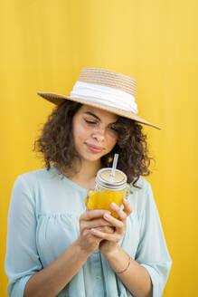 Porträt einer Frau mit Strohhut, die Saft trinkt, gelber Hintergrund - AFVF03664