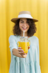 Porträt einer Frau mit Strohhut, die Saft trinkt, gelber Hintergrund - AFVF03666