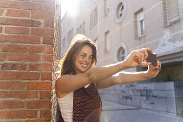 Junge Frau lehnt an einer Backsteinmauer und macht ein Selfie - AFVF03708