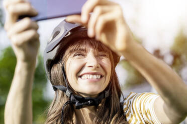 Glückliche Frau mit Fahrradhelm macht ein Selfie - FMKF05772
