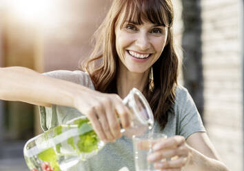 Porträt einer glücklichen Frau, die Wasser in ein Glas gießt - FMKF05774