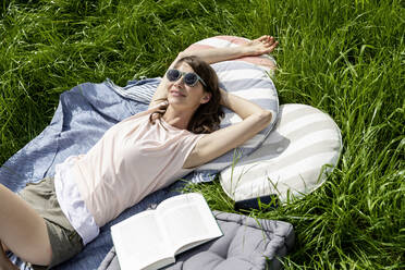 Entspannte Frau mit Buch auf einer Wiese liegend - FMKF05776