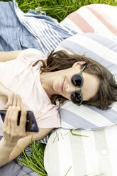 Entspannte Frau, die auf einer Wiese liegt und ein Mobiltelefon benutzt - FMKF05779