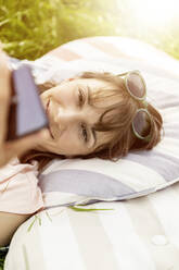 Entspannte Frau, die auf einer Wiese liegt und ein Mobiltelefon benutzt - FMKF05783