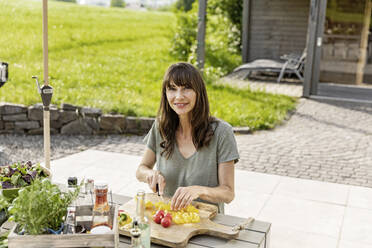 Porträt einer lächelnden Frau, die einen Salat auf einem Gartentisch zubereitet - FMKF05785