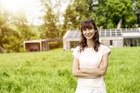 Porträt einer lächelnden Frau, die auf einer Wiese vor einem Haus steht, lizenzfreies Stockfoto