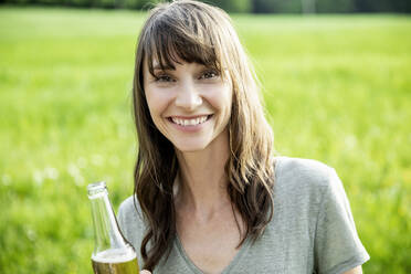 Portrait of smiling brunette woman with a beer bottle outdoors - FMKF05798