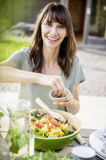 Porträt einer lächelnden Frau, die einen Salat auf einem Gartentisch zubereitet - FMKF05802