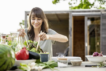 Smiling woman preparing a salad on garden table - FMKF05806