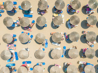 ACHAIA, GREECE - JULY 2018: Aerial view of vacationers on beach under straw parasols. - AAEF00201