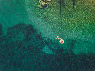 Luftaufnahme einer schwimmenden Frau mit zwei Kindern auf einer aufblasbaren Matratze auf der Insel Trizonia, Griechenland. - AAEF00218