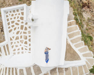 Luftaufnahme Frau auf dem Dach liegend auf Santorini traditionelles Haus mit umlaufender Treppe, Griechenland. - AAEF00468
