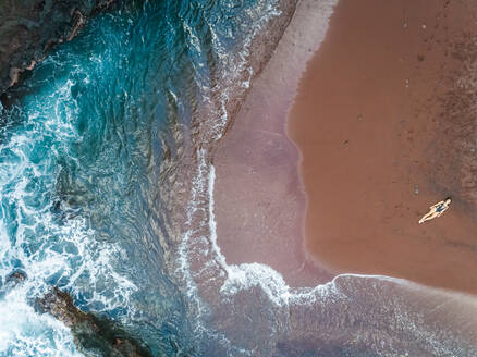 Aerial view of an attractive woman sunbathing on red sand beach, Hawaii, U.S.A. - AAEF00650