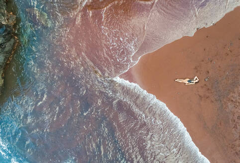 Aerial view of an attractive woman sunbathing on red sand beach, Hawaii, U.S.A. - AAEF00652