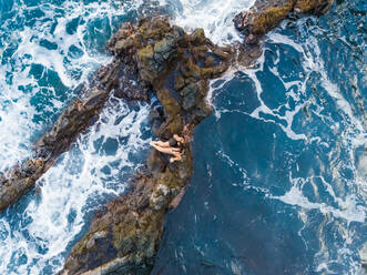 Luftaufnahme einer Frau, die auf einer Felsformation an der Küste sitzt, Hawaii, U.S.A. - AAEF00655