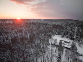 Luftaufnahme eines schneebedeckten Hauses auf dem Lande bei Sonnenuntergang in Estland. - AAEF00892