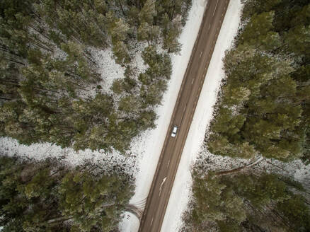 Luftaufnahme eines Autos, das allein durch einen verschneiten Wald in Estland fährt. - AAEF01045