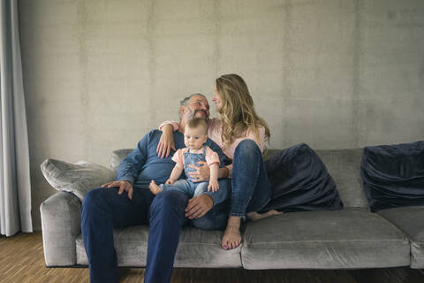 Glückliche dreiköpfige Familie, die zu Hause auf der Couch sitzt, lizenzfreies Stockfoto