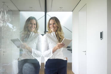 Smiling businesswoman holding tablet in modern home - MOEF02402