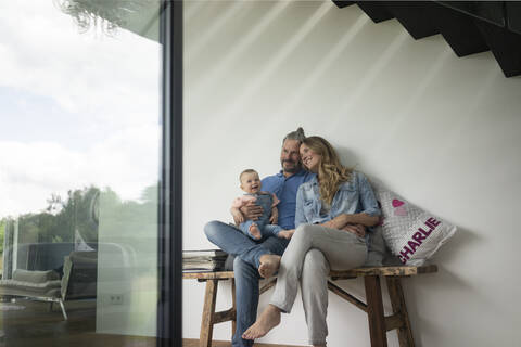 Glückliche dreiköpfige Familie, die zu Hause auf einer Bank sitzt, lizenzfreies Stockfoto