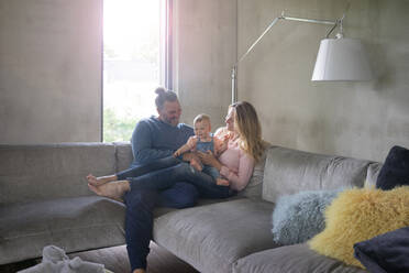 Happy family of three sitting on couch at home - MOEF02454