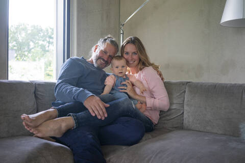 Porträt einer glücklichen dreiköpfigen Familie, die zu Hause auf der Couch sitzt, lizenzfreies Stockfoto