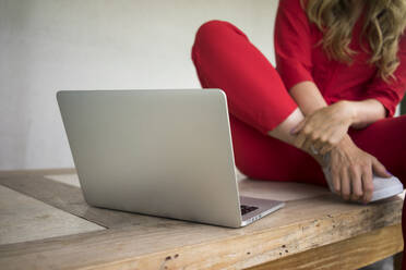 Nahaufnahme einer Frau mit Laptop, die zu Hause auf einem Holztisch sitzt - MOEF02458