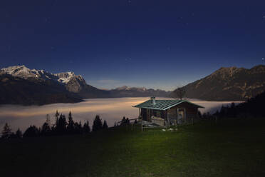 Log cabin at Mt. Wank with beautiful Mount Zugspitze and cloudscape at night, Bavaria, Germany - RUEF02305