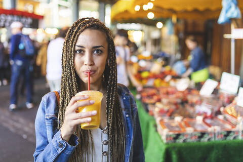 Portrait of young woman drinking fresh orange juice on street market, London, UK stock photo