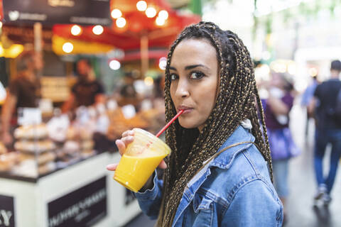 Porträt einer jungen Frau, die auf einem Straßenmarkt frischen Orangensaft trinkt, London, UK, lizenzfreies Stockfoto
