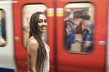 Porträt einer lächelnden jungen Frau, die am Bahnsteig einer U-Bahn-Station wartet, London, Vereinigtes Königreich - WPEF01692