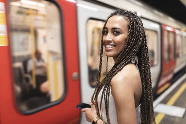 Porträt einer glücklichen jungen Frau, die am Bahnsteig einer U-Bahn-Station wartet, London, Vereinigtes Königreich - WPEF01695