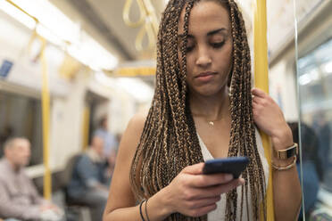 Porträt einer jungen Frau, die im U-Bahn-Zug auf ihr Handy schaut, London, UK - WPEF01697