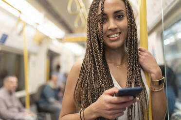 Porträt einer lächelnden jungen Frau mit Handy in einem U-Bahn-Zug, London, UK - WPEF01698