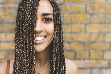 Portrait of happy young woman with long braids in front of brick wall - WPEF01708