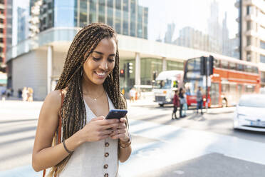 Portrait of smiling young woman in the city looking at cell phone, London, UK - WPEF01711