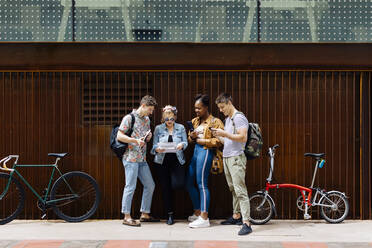 Studenten stehen auf der Straße, halten Smartphones in der Hand und lesen Zeitung - SODF00063