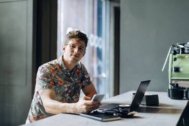 Young man sitting in cafe, using samrtphone and laptop - SODF00079