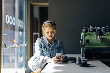 Junge Frau in einem Café, die ein Smartphone benutzt und Fotos macht - SODF00084