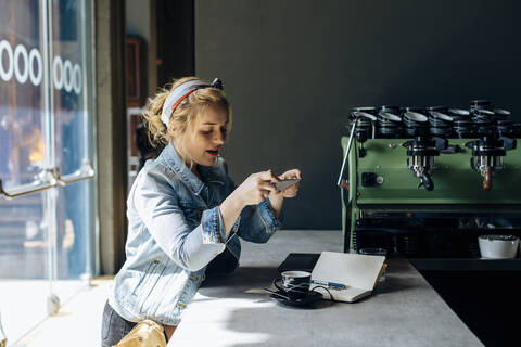 Junge Frau in einem Café, die ein Smartphone benutzt und Fotos macht, lizenzfreies Stockfoto