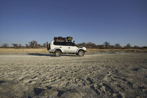 Weißer Geländewagen mit Affenbrotbäumen im Hintergrund gegen den klaren Himmel, Makgadikgadi Pans, Botswana - VEGF00445