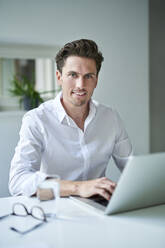 Porträt eines lächelnden Geschäftsmannes mit Laptop im Büro - PNEF01783