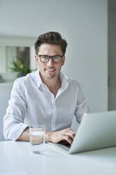 Portrait of smiling businessman using laptop in office - PNEF01784