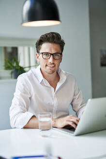 Portrait of smiling businessman using laptop in office - PNEF01785