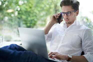 Geschäftsmann am Telefon mit Laptop im Büro - PNEF01788