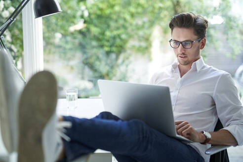 Porträt eines Geschäftsmannes, der im Büro an einem Laptop arbeitet - PNEF01792