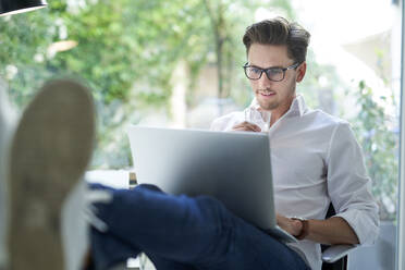 Porträt eines lächelnden Geschäftsmannes mit Laptop im Büro - PNEF01794