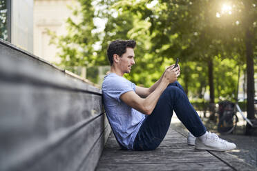 Man sitting on bench using smartphone - PNEF01809