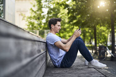 Mann sitzt auf einer Bank und benutzt ein Smartphone - PNEF01809