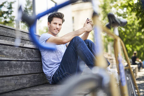 Porträt eines Mannes mit Rennrad auf einer Bank sitzend und sich ausruhend - PNEF01811